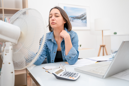 Woman sitting in office with fan blowing on her face from broken AC
