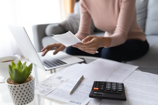 A looking at a piece of paper and laptop with a calculator on the table in front of her.