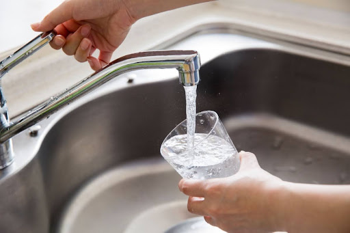 A person using a kitchen sink faucet to fill a water glass.